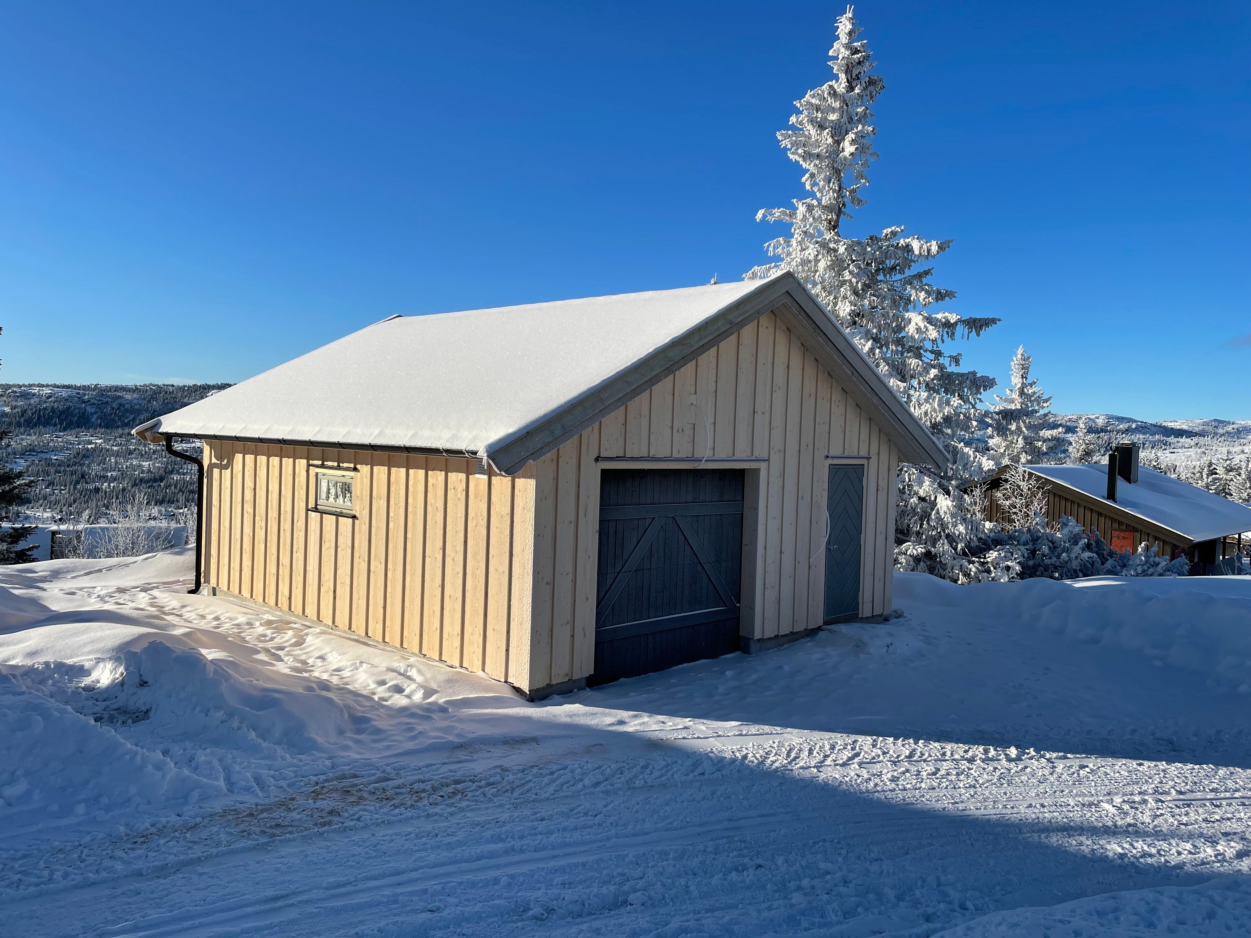 Garasje med svart port i snø, med utsikt over dalen