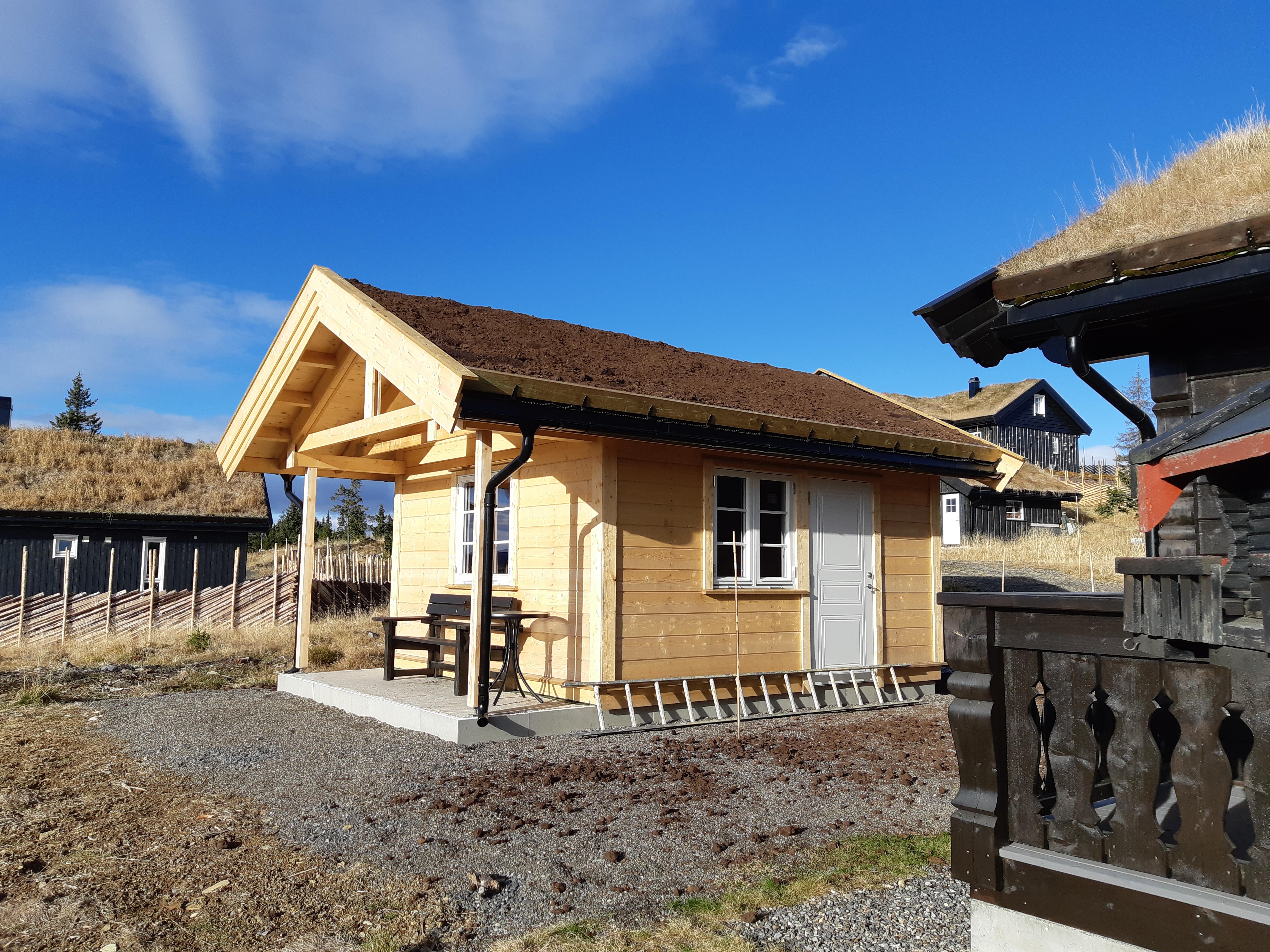 Liten hytte i lys trepanel med overbygd inngangsparti